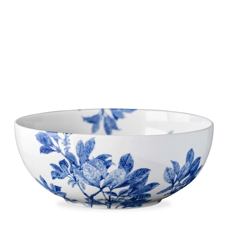 The CASKATA ARBOR VEGETABLE SERVING BOWL is a white ceramic bowl with a blue floral and leafy pattern on the exterior, some of which extends inside. Its blue and white porcelain design evokes classic vintage tableware. Brand: CASKATA.