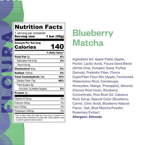 A green and purple FLOURA & CO box labeled "BLUEBERRY MATCHA FLOURS FIBERCRUSH BAR 2" sits behind a matching fruit bar. The packaging highlights 13g prebiotic fiber, dietary benefits, and its value as a gut health snack.