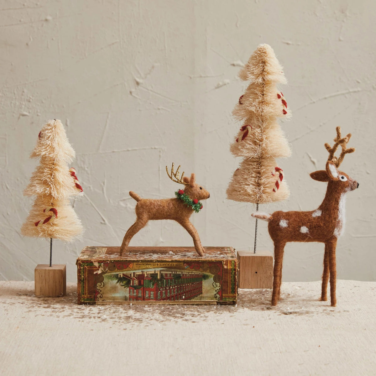 Create a festive scene with CREATIVE COOP FELT STANDING DEER and cream-colored decorative trees with red accents, artfully arranged on a vintage-style box—perfect for seasonal home decor.
