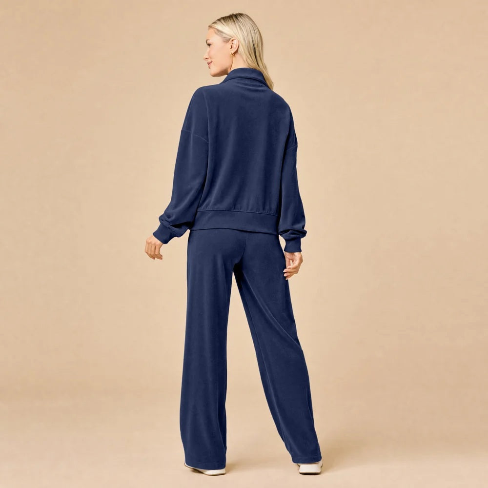 A woman seated on the floor wearing a Softies - Serenity 1/4 Zip Top with Wide Leg Pant lounge set in midnight, featuring a navy blue quarter-zip pullover and matching wide-leg lounge pants.