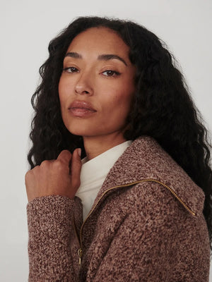 A person wearing a VARLEY - SHERIDA HALF-ZIP KNIT SWEATER IN GINGERBREAD FLECK, a brown speckled boucle yarn sweater with a collared half-zip neckline.