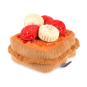 Close-up of the PLAY PET LIFESTYLE THICK ‘N FLUFFY FRENCH TOAST DOG TOY on a brown fabric with red and white patterns, pictured with plush strawberry and muffin toys.