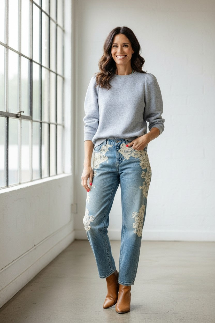 A person with long hair embraces comfort and individuality, wearing a KMJ SHIRTS Cooper Sweatshirt in gray with a white bow. Metallic sequin pants and silver shoes complete the look as they stand among disco balls on the floor against a plain background.