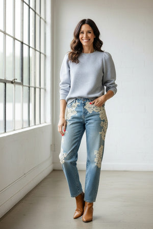 A person with long hair embraces comfort and individuality, wearing a KMJ SHIRTS Cooper Sweatshirt in gray with a white bow. Metallic sequin pants and silver shoes complete the look as they stand among disco balls on the floor against a plain background.
