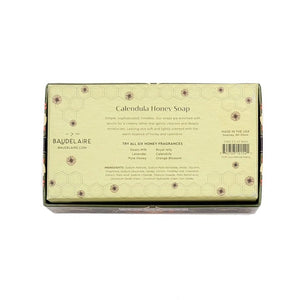 A beautifully packaged BAUDELAIRE Calendula Honey Soap Gift Box includes two 3.5 oz hexagonal green bars with an embossed beehive motif, partially displayed from a decorative floral box labeled “Calendula.” This elegant BAUDELAIRE gift set features triple-milled soap for a luxurious and gentle cleansing experience.