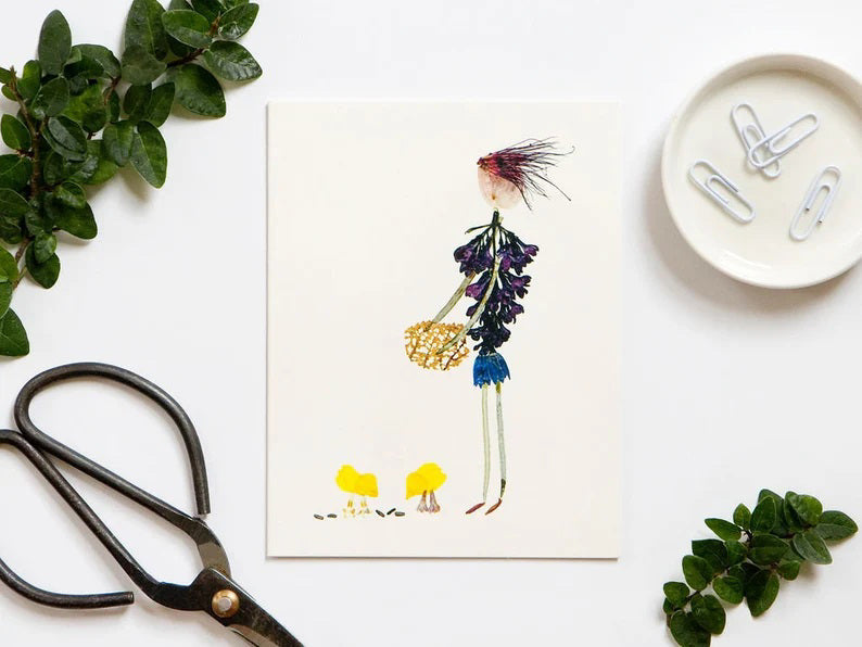 The PETAL PEOPLE PRESS - BARNYARD PARTY CARD features a person and two chicks made from pressed flowers. With a purple flower torso, green stem legs, pink petal head holding a yellow flower basket, and yellow chicks with orange legs, it's perfect for country-themed occasions.