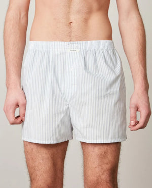 A person models HARTFORD - COTTON BOXER SHORTS in light blue and white stripes with an elastic waistband, standing against a plain beige background.