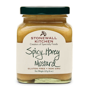 A jar of STONEWALL KITCHEN - SPICY HONEY MUSTARD sits on a slate board surrounded by puff pastry bites, accompanied by a bowl of this sweet and spicy mustard dipping sauce and wooden forks, all arranged on a woven placemat atop a wooden table.