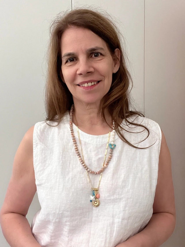 The SANDRINE FRANCE STUDIO - SOLANA NECKLACE is a handmade gold chain from NYC, featuring five charms: a porcelain dove, textured gold disc, two turquoise beads, green oval bead, and peach teardrop, shown on a white background.
