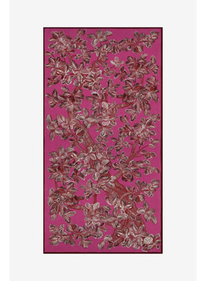 A person stands against a plain beige background wearing a long cream-colored sweater dress and the INOUI EDITIONS - ARBORIS WOOL SCARF IN PINK by INOUI, a bright pink, 100% wool scarf featuring large floral patterns and made in India.