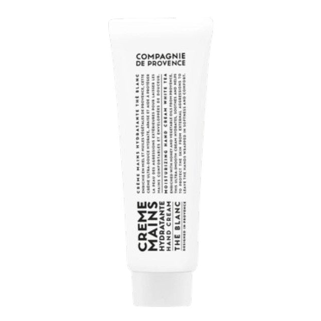 A bottle of Savon Liquide de Marseille soap, crafted with nourishing Provence plant oils, and a tube of COMPAGNIE DE PROVENCE - TRAVEL HAND CREAM WHITE TEA 1OZ by CIE LUXE BRANDS rest on a round tray atop a wooden stool, set against a backdrop of beige tiles.