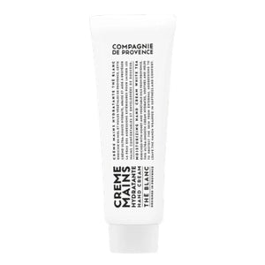 A bottle of Savon Liquide de Marseille soap, crafted with nourishing Provence plant oils, and a tube of COMPAGNIE DE PROVENCE - TRAVEL HAND CREAM WHITE TEA 1OZ by CIE LUXE BRANDS rest on a round tray atop a wooden stool, set against a backdrop of beige tiles.