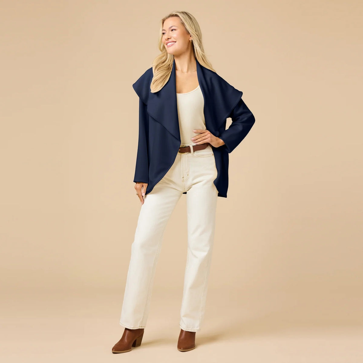 A woman wears an off-white SOFTIES - DREAMTECH EXAGGERATED COLLAR CARDIGAN with an exaggerated waterfall collar, cinched at the waist with a thin belt, and holds a matching handbag.
