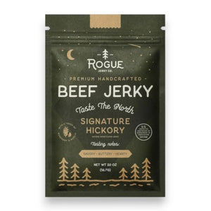 A dark green pouch of ROGUE JERKY - HICKORY BEEF JERKY by ROGUE JERKY CO., featuring forest and moon imagery, labeled “Premium Handcrafted” and “Taste The North.” This savory, buttery, hearty sugar free jerky is an ideal keto friendly snack. Net weight: 2 oz.