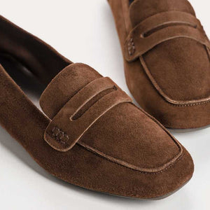 The REQINS HEMA suede loafer in cacao features moccasin-style stitching, a penny strap, and a low black heel for stylish comfort, showcased on a light background.