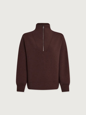 A person wears an oversized, dark brown VARLEY - HAWLEY HALF-ZIP SWEATSHIRT IN COFFEE BEAN MARL with a gold zipper.