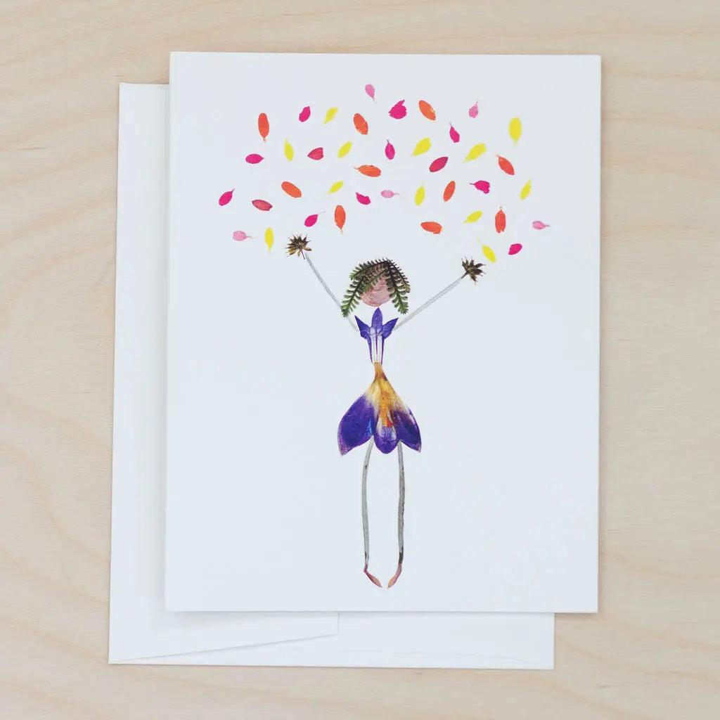 The PETAL PEOPLE PRESS - CONFETTI CARD by PETAL PEOPLE PRESS features a stick figure made from pressed flowers and leaves with colorful petals above, surrounded by green leaves and office accessories on a white surface.