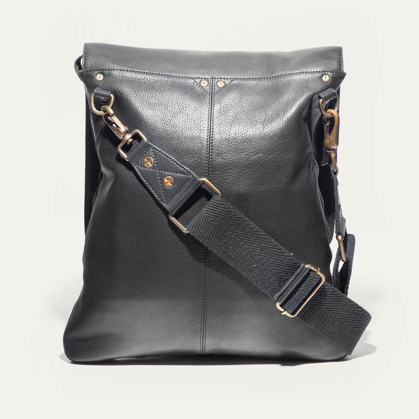 The WILL LEATHER GOODS OTTO Crossbody Bag in black full-grain leather features a front flap, gold-tone hardware, adjustable shoulder strap, and a small stitched patch on the lower right corner. Displayed against a plain white background.