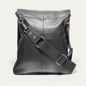 The WILL LEATHER GOODS OTTO Crossbody Bag in black full-grain leather features a front flap, gold-tone hardware, adjustable shoulder strap, and a small stitched patch on the lower right corner. Displayed against a plain white background.