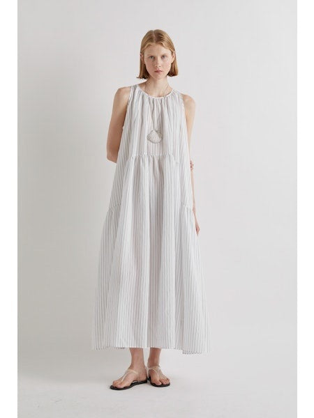 A person stands against a plain white background, wearing the MEIMEIJ Sleeveless Maxi Dress with Stripes, an ankle-length summer piece styled with flat sandals and a statement necklace for an effortlessly chic look.