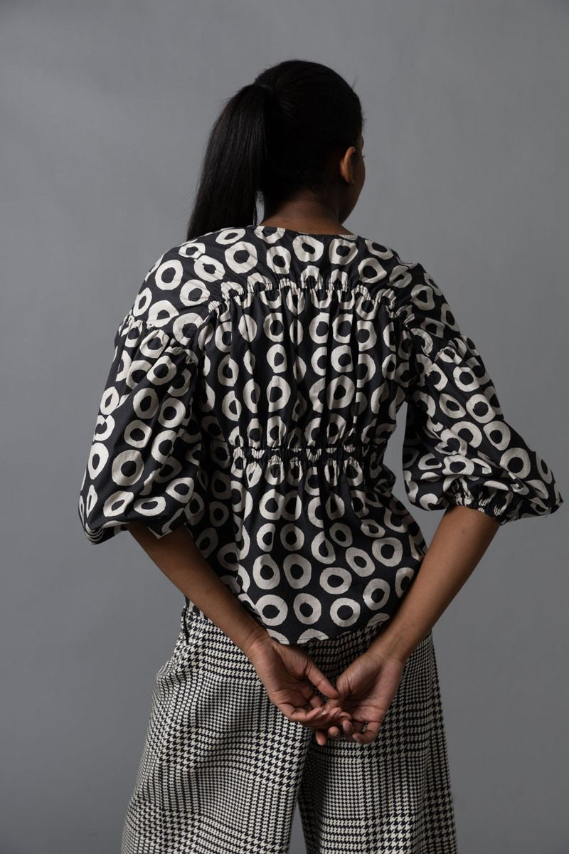 A person with long brown hair, seen from behind, wears the HOPE FOR FLOWERS Shirred Blouse and loose, dark green cargo pants with large pockets, standing against a plain gray background.