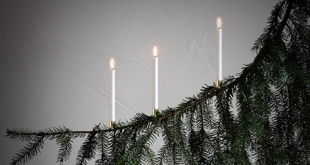 A close-up of a Christmas tree decorated with PIFFANY’s UYUNI White Mini Taper Candles with Clips (0.5x5.4), held by gold candle clips and accented with red-and-white woven heart ornaments, set against a dark background.