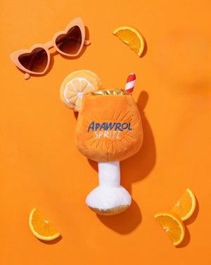 The HAUTE DIGGITY DOG APAWROL SPRITZ DOG TOY is a plush, squeaky dog toy shaped like an orange cocktail glass, featuring "APAWROL SPRITZ" embroidery, a slice of orange on top, and a red-striped straw.