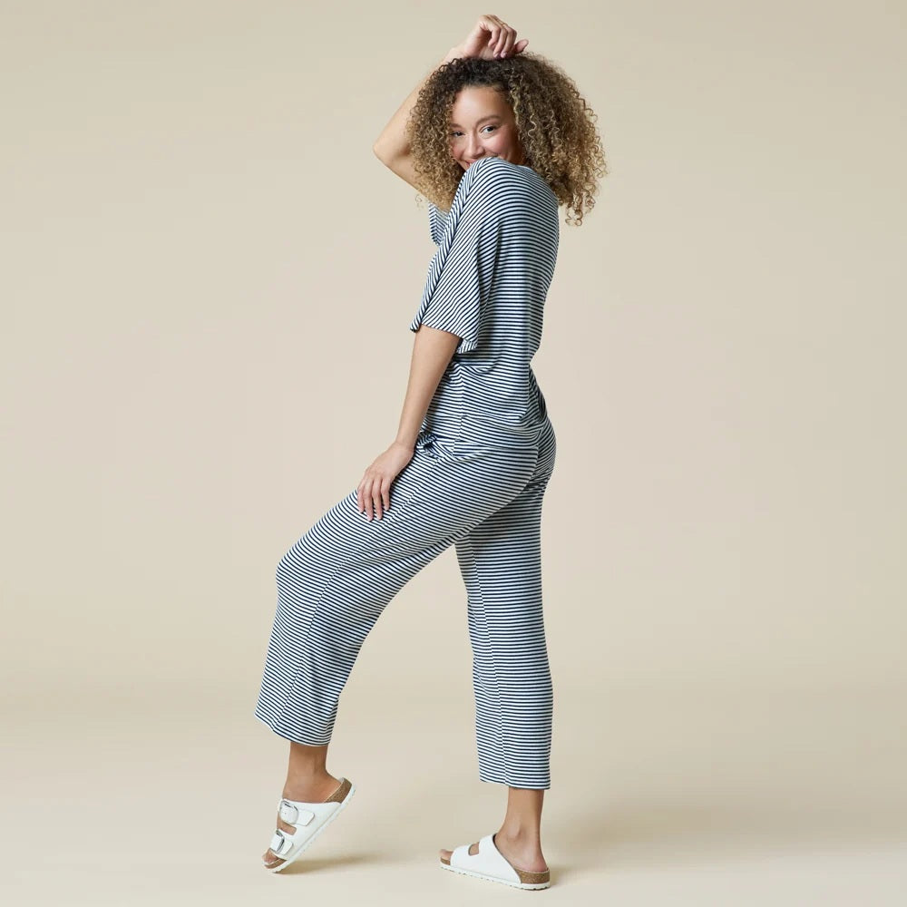 A woman wearing a light blue and white striped SOFTIES - DREAM RELAXED V-NECK WITH CAPRI LOUNGE SET with a V-neck, capri-length pants, and white sneakers.