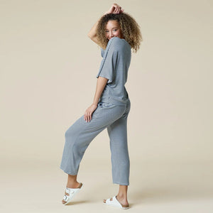 A woman wearing a light blue and white striped SOFTIES - DREAM RELAXED V-NECK WITH CAPRI LOUNGE SET with a V-neck, capri-length pants, and white sneakers.