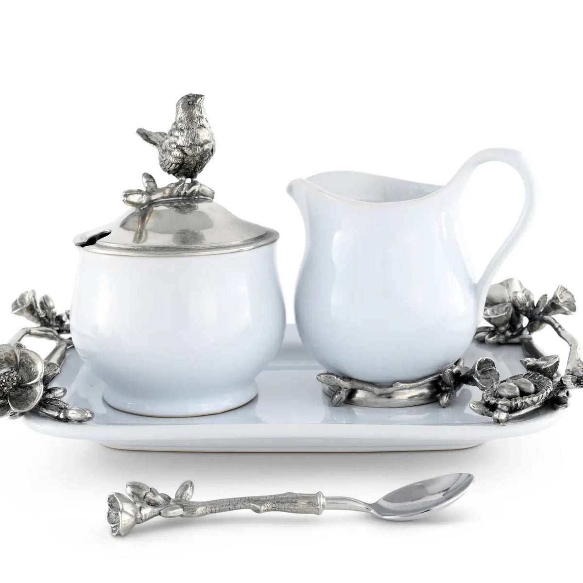 The VAGABOND HOUSE - SONG BIRD CREAMER SET by VAGABOND HOUSE includes a white ceramic sugar bowl and creamer, each with ornate silver floral handles and a bird-shaped lid handle. The elegant set also features a decorative tray and a small spoon with a floral handle for stylish serving.