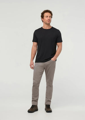 Close-up of the back of a person wearing DUER No Sweat Athletic Taper Pants in Stone, featuring two back pockets and a tan leather DUER patch on the waistband. They're also wearing a black shirt.