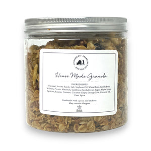 A clear plastic container with a silver lid, labeled "Fearrington Signature Collection - Fearrington Housemade Granola." The label lists ingredients such as oatmeal, sesame seeds, and various nuts. Brimming with gourmet granola, the container is set against a plain white background.