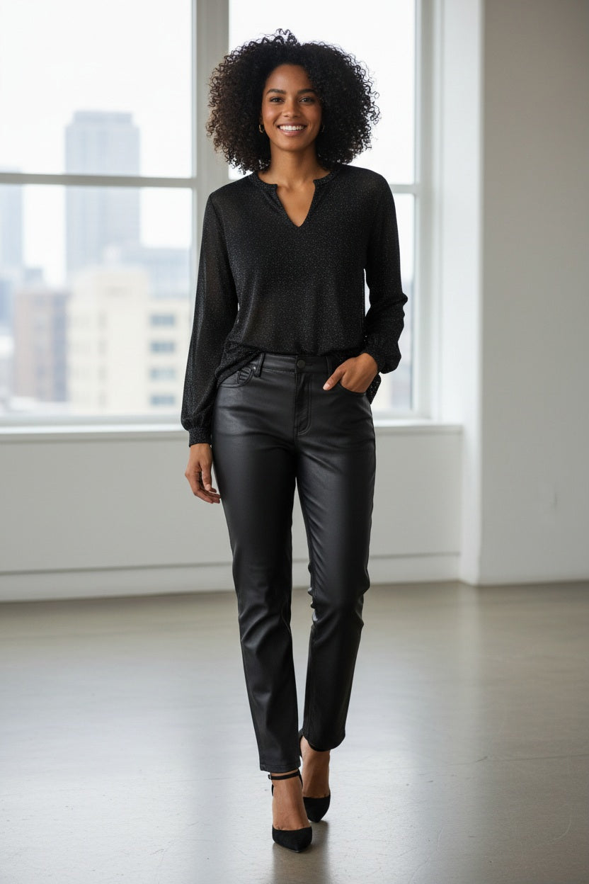 A woman with long brown hair wears the KINROSS CASHMERE SHIMMER SPLITNECK TOP, a semi-sheer black blouse with subtle lurex sparkles, paired with black leather pants against a plain white background.