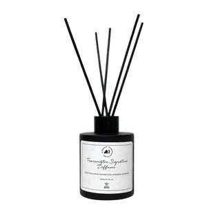 Housed in a sleek black bottle with five slender black reeds, the FEARRINGTON SIGNATURE DIFFUSER from the FEARRINGTON SIGNATURE COLLECTION by FEARRINGTON VILLAGE - HOME DECOR features a white label displaying "Fragrance Signature Diffuser" and scent notes of cedarwood, lavender, and amber. Inspired by the tranquil allure of Fearrington Village, this sophisticated reed diffuser is ideal for anyone who appreciates the calming atmosphere created by a lavender candle.