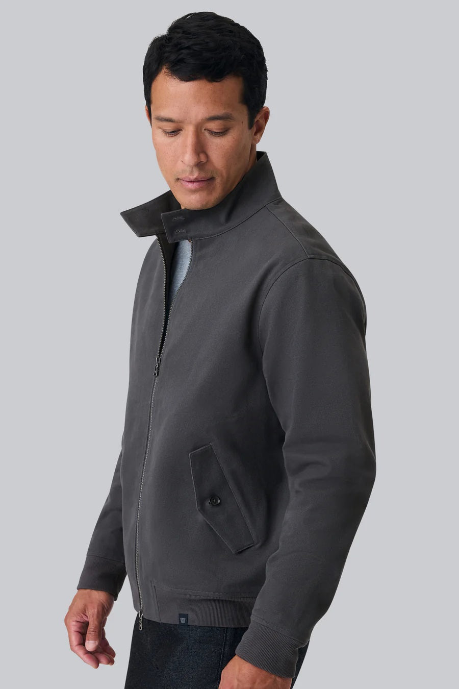 The MACK WELDON Twill Harrington Jacket in Asphalt is a dark gray cotton cavalry twill zip-up with a stand collar, two angled button-flap pockets, ribbed cuffs and hem, offering an English jacket style. Shown on a black background.