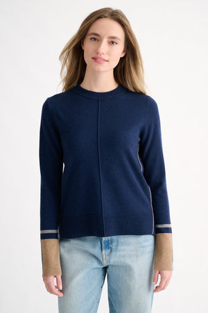 A person wearing the KINROSS CASHMERE Colorplay Crew Neck Cashmere Sweater in navy, featuring tan and gray cuffs and a classic crew neckline, pairs it with light blue jeans while standing against a plain white background and looking at the camera with a slight smile.