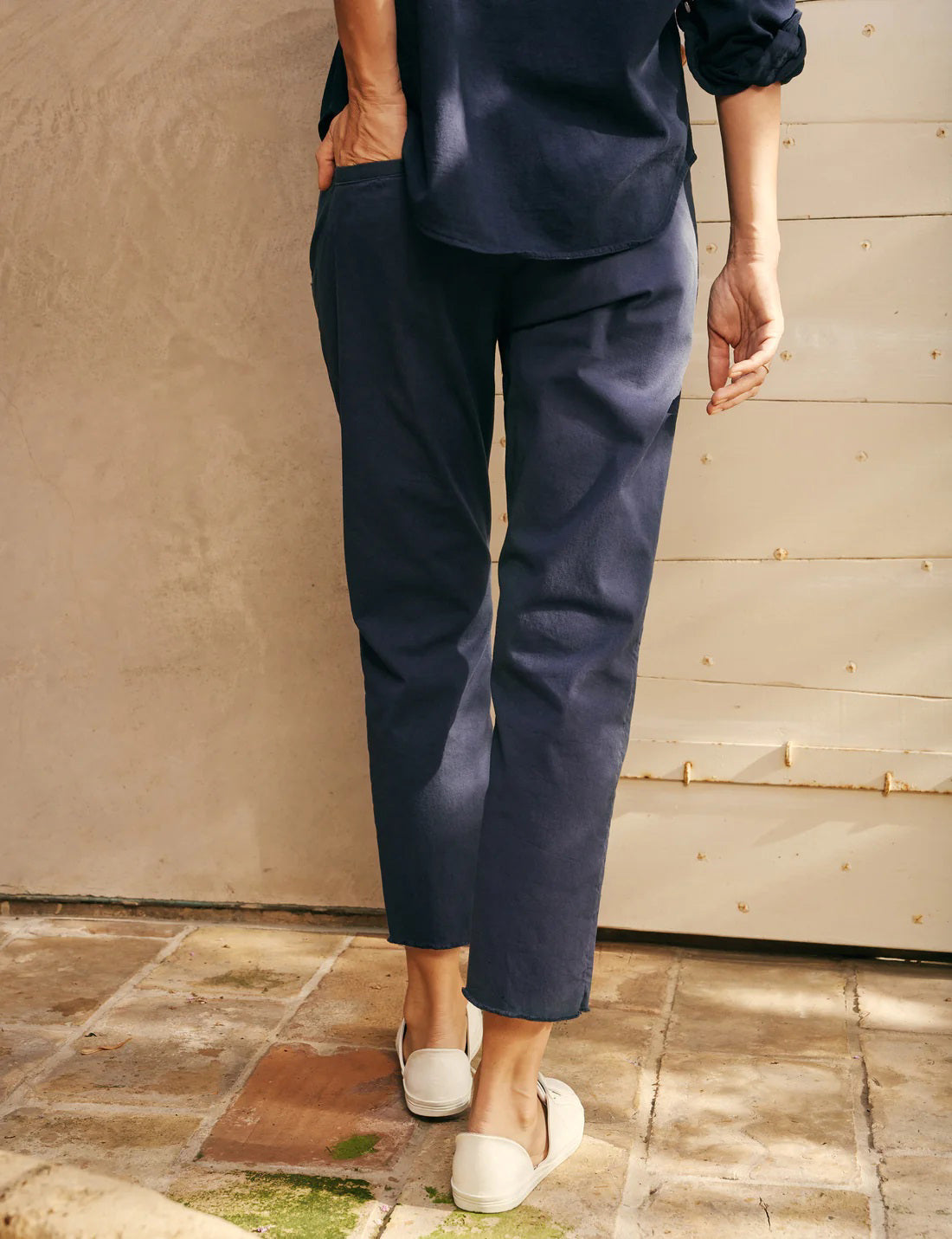 A pair of FRANK &amp; EILEEN’s THE WICKLOW Italian Chinos in Performance Twill, featuring a navy blue color, straight legs, and raw unfinished hems, is laid flat on a light textured background for an Italy-meets-California vibe.