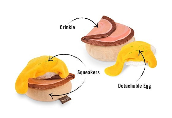 Introducing the PLAY PET LIFESTYLES/BRANDS BARKING BRUNCH - BENNY’S BENEDICT: an adorable dog toy designed to look like a plush egg with a yellow yolk atop a round, brown base, mimicking a classic brunch favorite. Perfect for playful pups, this fun and charming brunch-themed toy features a black fabric tag attached at the bottom.