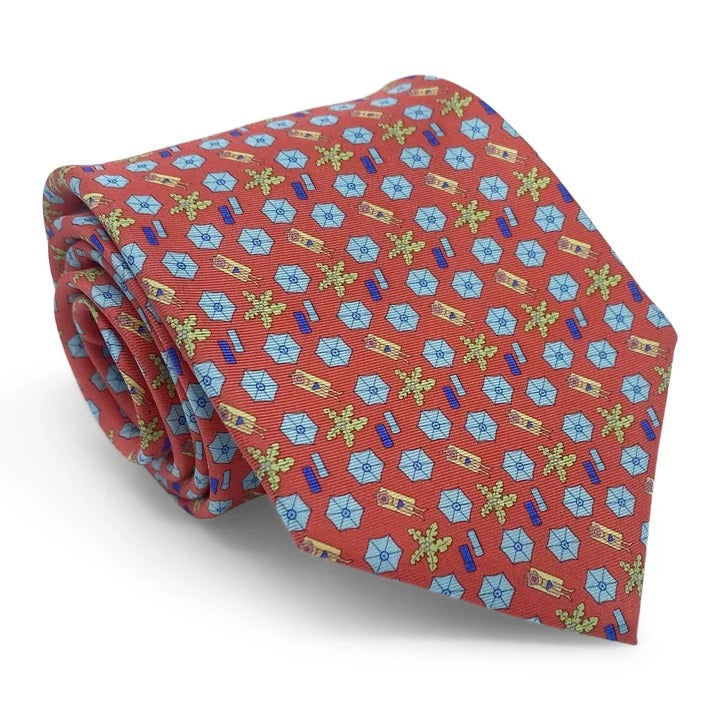 A rolled-up red necktie featuring a repeating pattern of pink beach umbrellas, yellow-green palm trees, and blue beach towels, the Peter-Blair Sunscreen Silk Tie by Bird Dog Bay is handmade in New York and finished with the signature Peter-Blair woven label.