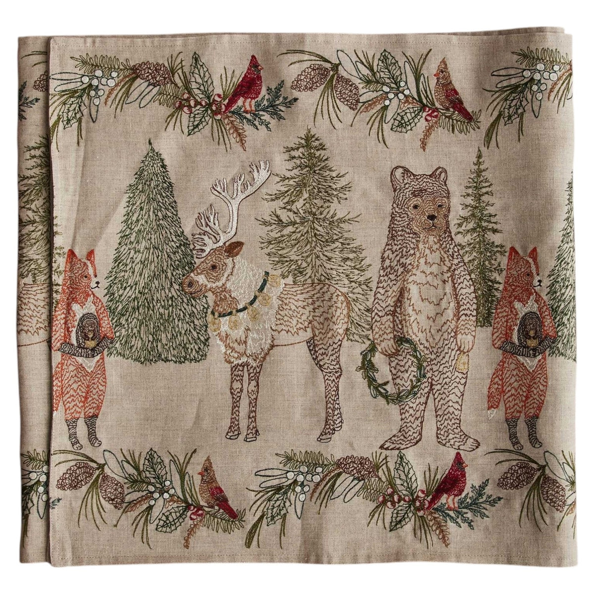 A CHRISTMAS CHEER EMBROIDERED LINEN TABLE RUNNER featuring woodland animals in winter attire and Christmas trees, draped over a wooden dining table set with plates, glassware, and candlesticks.