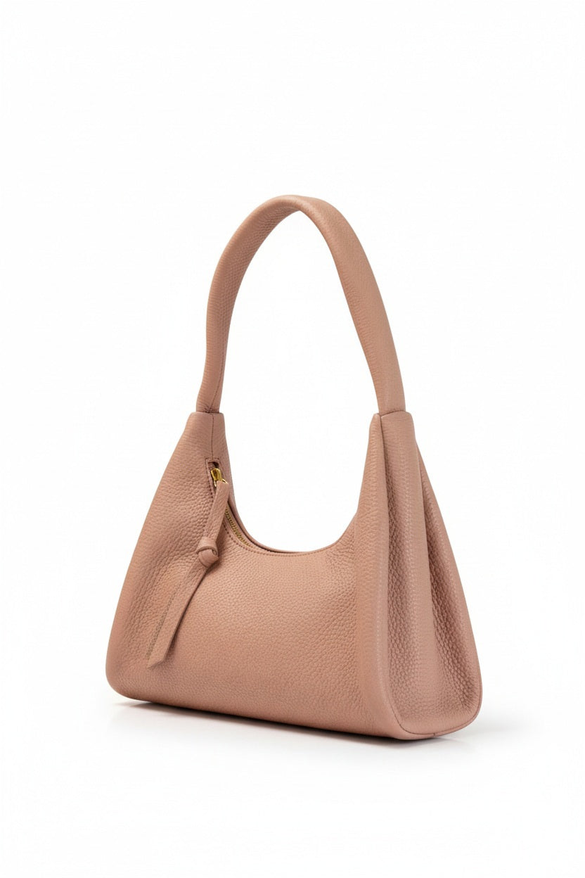 The OLIVEVE Gia Baguette Handbag in nude Italian buffalo cowhide features a pebbled texture and curved handle. It's ethically made with a zipper closure, leather pull tab, and set against a white background.