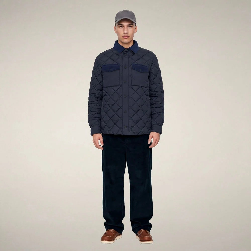 The SAVE THE DUCK - FIRMIN Puffer Jacket in Blue Black by SAVE THE DUCK features a diamond-quilted design, long sleeves, snap button closures, two chest pockets with flaps, and a dark collar, presented against a plain light background.