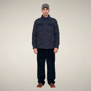 The SAVE THE DUCK - FIRMIN Puffer Jacket in Blue Black by SAVE THE DUCK features a diamond-quilted design, long sleeves, snap button closures, two chest pockets with flaps, and a dark collar, presented against a plain light background.