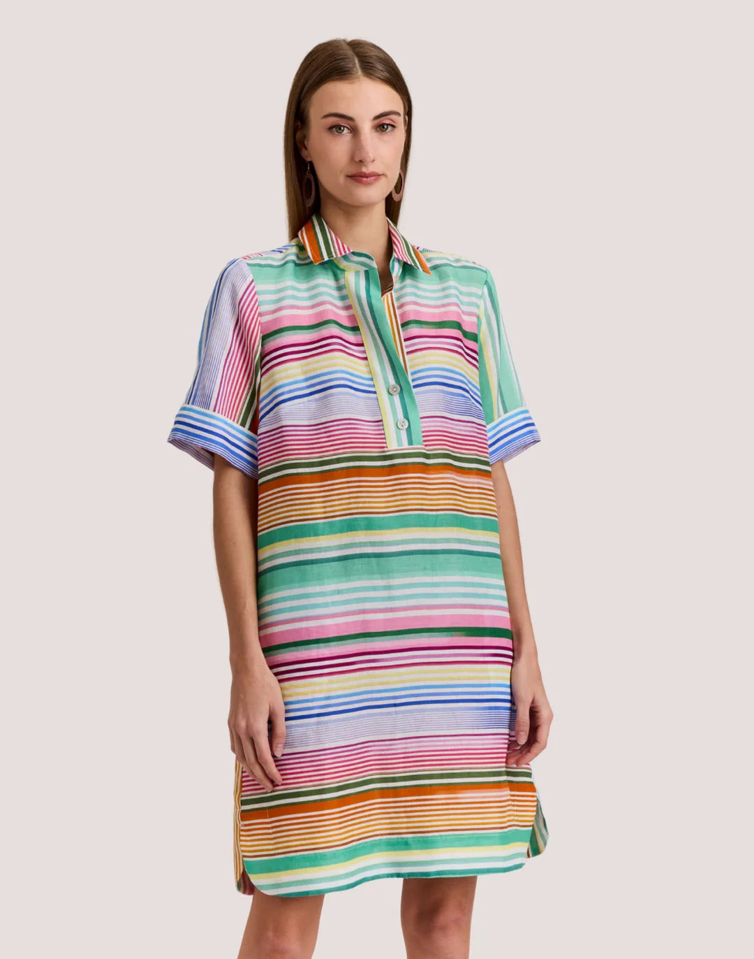 A woman wears the HINSON WU AILEEN Short Sleeve Linen Dress in Multi Stripe, a knee-length design with colorful stripes, a collar, front buttons, and pockets.