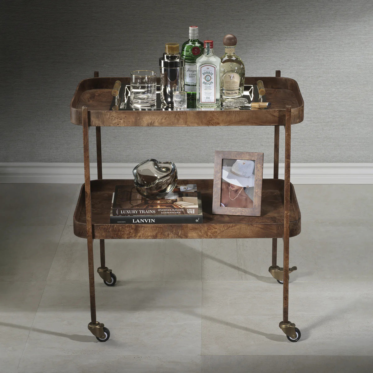 The BENETEAU BAR CART IN BURL WOOD VENEER by ZODAX features a two-tier rectangular design with raised edges, a brown burl veneer finish, and four caster wheels for mobility. Its vintage, elegant style is available for in-store pickup.