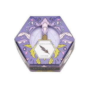 Hexagonal BAUDELAIRE - LAVENDER HONEY SOAP 3.5 OZ bars, each in decorative, colorful BAUDELAIRE-branded hex boxes, are arranged in a honeycomb pattern on a white surface. The soaps display unique designs and vibrant colors, with some unwrapped to reveal the luxurious triple-milled texture and enticing lavender honey fragrance.