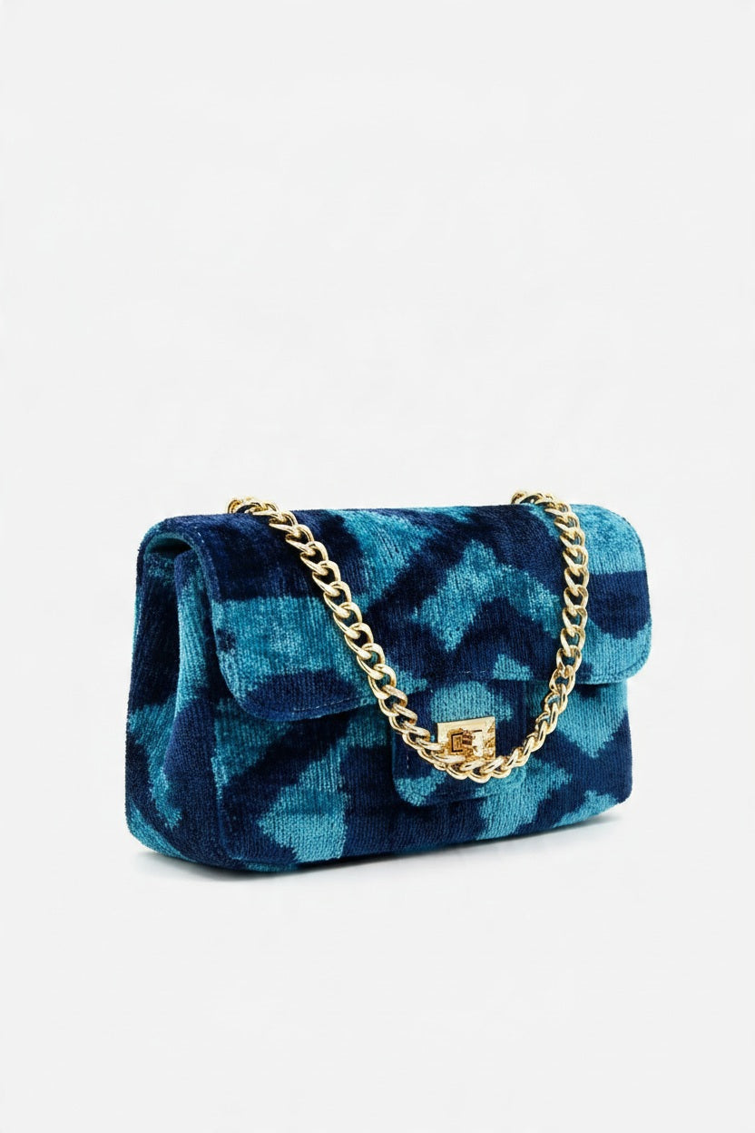 BALDIZ - BROOKE CLUTCH CROSSBODY BAG IN MIDNIGHT BLUE, a patterned silk velvet clutch featuring a gold chain shoulder strap and a gold rectangular clasp.