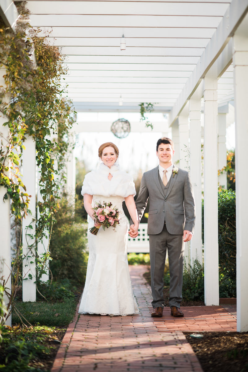 Wedding couple standing under a white arbor with greenery.