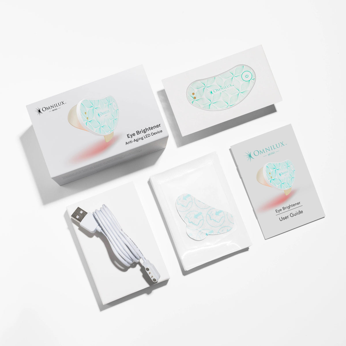 A crescent-shaped Omnilux Eye Brightener Kit is shown against a light gray background, featuring a power button and branding text. The device has a leaf pattern and emits a subtle red glow, highlighting its red light therapy benefits for collagen production under the eyes.
