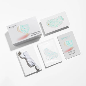A crescent-shaped Omnilux Eye Brightener Kit is shown against a light gray background, featuring a power button and branding text. The device has a leaf pattern and emits a subtle red glow, highlighting its red light therapy benefits for collagen production under the eyes.